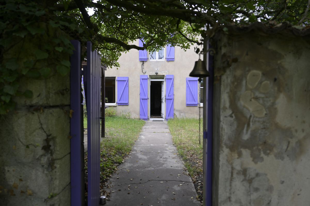 Le portail violet ouvert sur l'allée qui mène à la maison aux volets lavande
