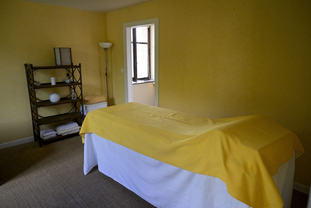 Une salle de soins aux murs jaunes, la table de massage couverte d'un drap jaune